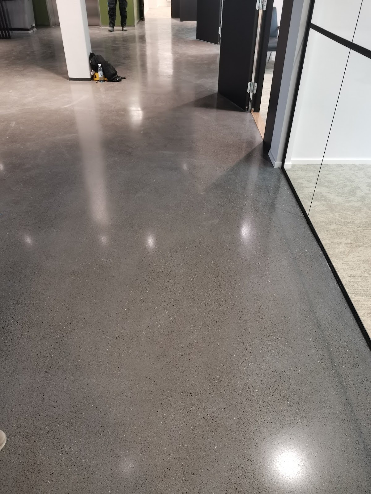 Kiiltävä harmaa lattiapinnoitus heijastaa valoja ja ympäristöä modernissa tilassa.
