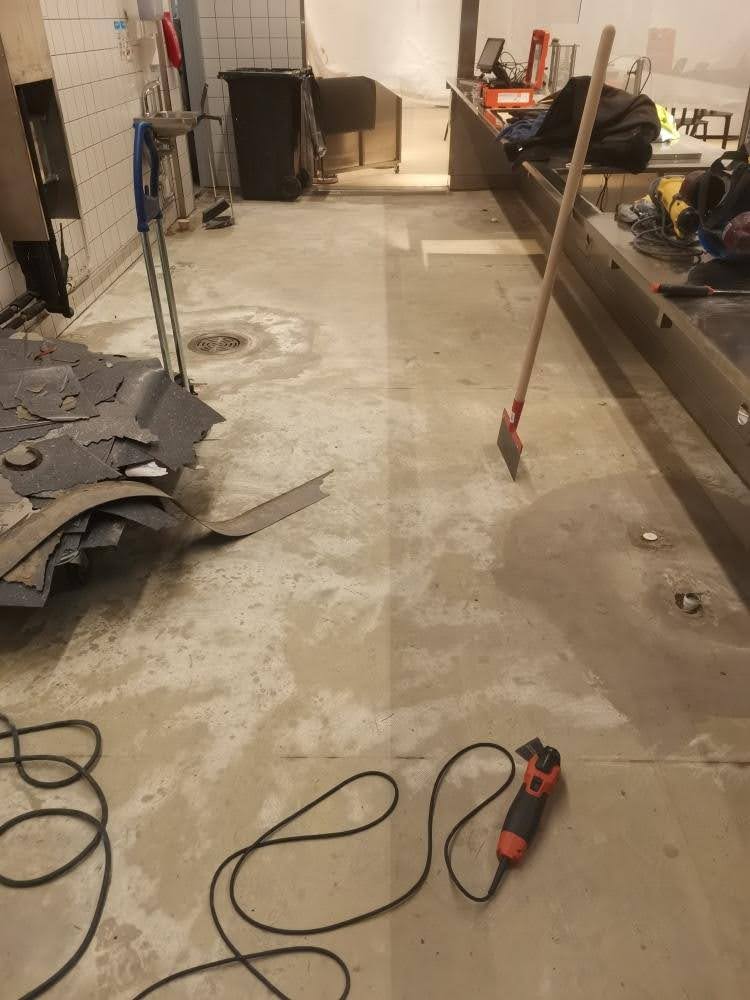 Lattiatyöt ovat käynnissä tilassa, jossa vanha lattiapinnoitus on poistettu ja työkaluja on lattialla.