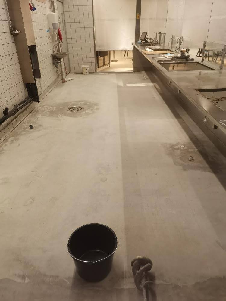 Betonilattia, jossa on lattiakaivo ja joka on valmis lattiapinnoitusta varten, näkyy tyhjässä tilassa.